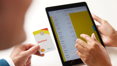 Person holding a Shell Card while using a tablet displaying a list of transactions with a yellow panel on the right.