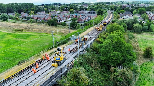 Rail workers and machinery carrying out track upgrades on an elevated railway line near a suburban neighbourhood.