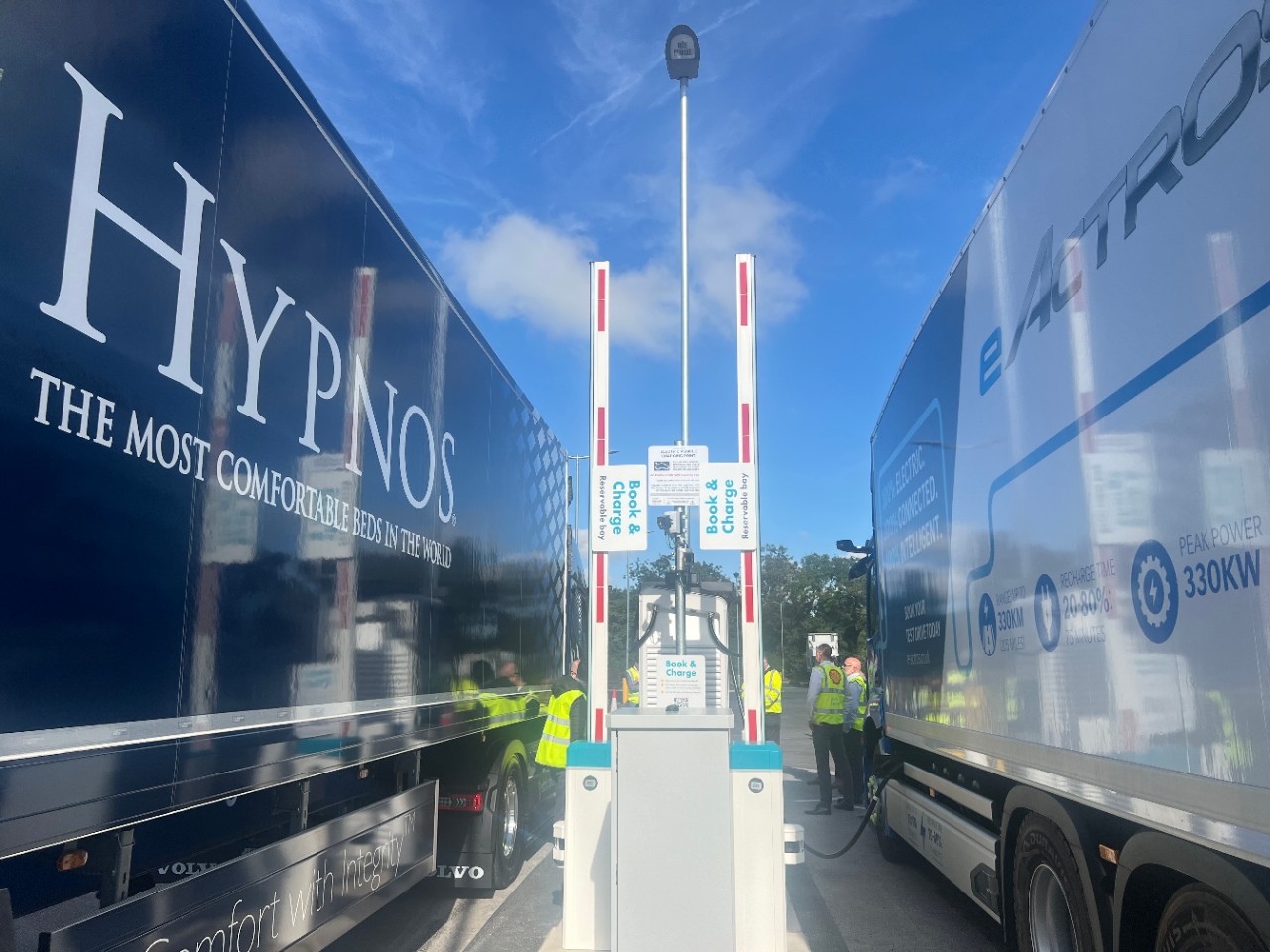 Two trucks parked in a book and charge bay; connected to an electric charge point.