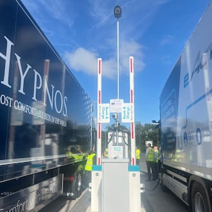 Two trucks parked in a book and charge bay; connected to an electric charge point.
