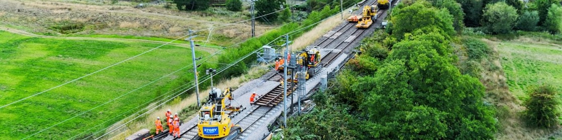 Rail workers and machinery carrying out track upgrades on an elevated railway line near a suburban neighbourhood.