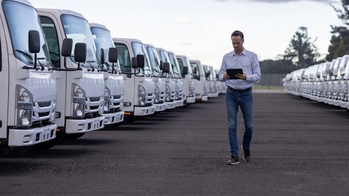 Person walking between two rows of white trucks while using a tablet in a fleet yard.