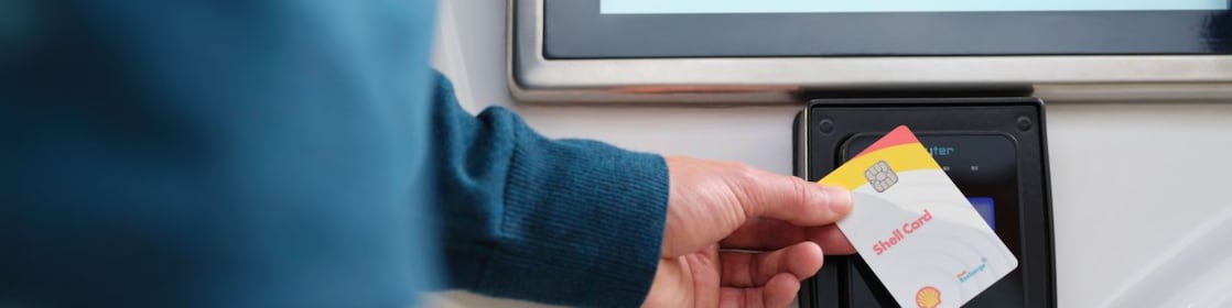 Close-up of a hand holding a Shell Card near a black payment terminal with a screen.
