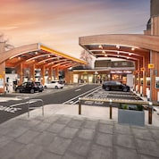 Modern Shell forecourt with timber canopy structure, fuel and electric charging bays, parked cars, and a convenience store.