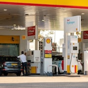 Shell forecourt showing V-Power petrol pumps and a Shell Hydrogen dispenser beneath a canopy, with two cars refuelling.