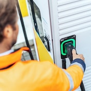 Close-up of a person in high-visibility clothing plugging an electric vehicle charging connector into a charging unit socket.