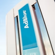 Close-up of a vertical blue “AdBlue®” label on a fuel pump, mounted between metallic panels.