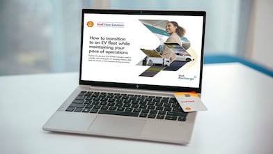 Two articulated lorries travelling in opposite directions on a divided highway bordered by trees under a clear blue sky.