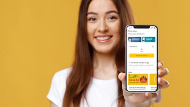 A person smiling holding a smartphone showing Shell app interface against a yellow background.