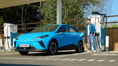 Man at electric vehicle charging stations with blue car