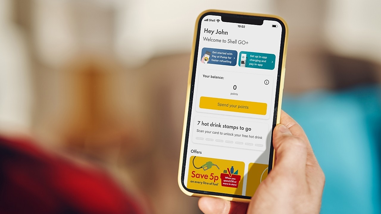 A person holding a phone,  open on the Shell App