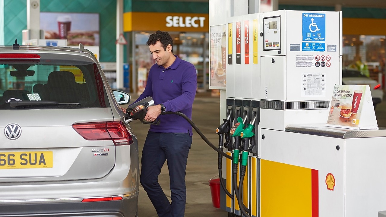 Image shows a man in a purple shirt and dark jeans refuelling his vehicle with Shell V-Power at a Shell service station.