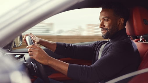 Man smiling in blue jumper driving a car with red seats