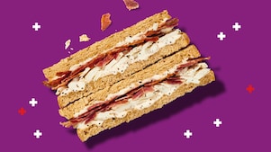 Tile showing deli by Shell chicken and bacon sandwich on a purple background with white and red plus sign confetti.