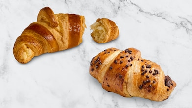 Two croissants on a white surface, one plain and one topped with chocolate pieces. A blue Co op “Proud to stock” logo appears in the top right corner.